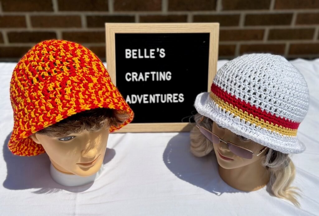 Acrylic Hat on the left, Cotton Hat on the right, with Belle's Crafting Adventures sign between them