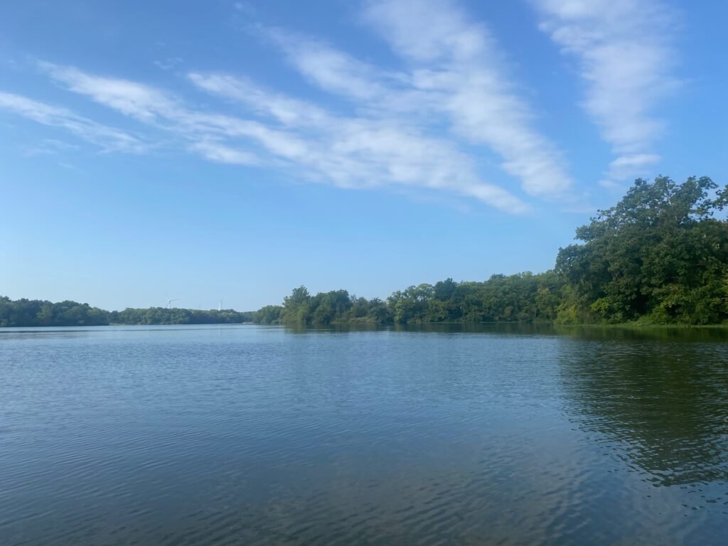 A partly cloudy day with a blue sky over a lake with some trees in the background